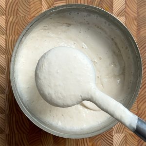 Gently stirring fermented dosa batter with ladle before making dosas, showing proper consistency and bubbles