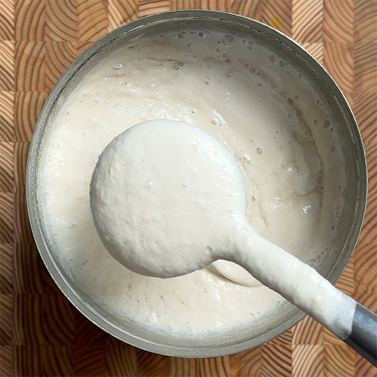 Gently stirring fermented dosa batter with ladle before making dosas, showing proper consistency and bubbles