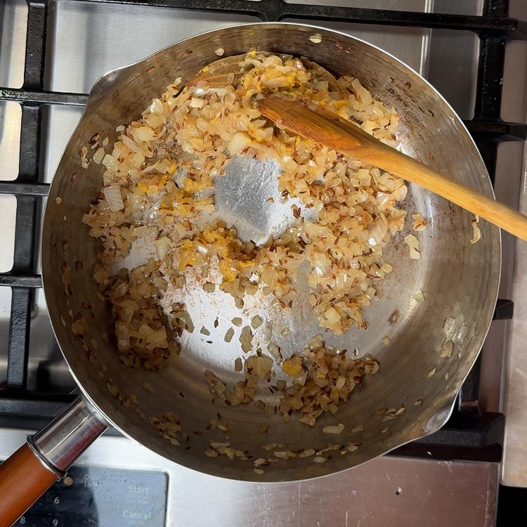 Golden brown onions in pan with fresh ginger garlic paste being stirred in