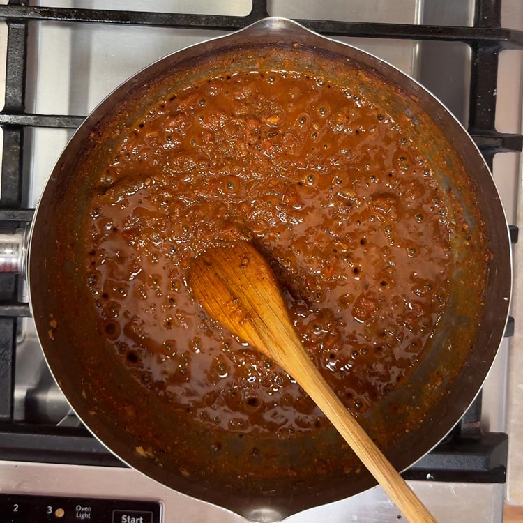 Rich brown curry base bubbling and simmering after adding bean cooking liquid