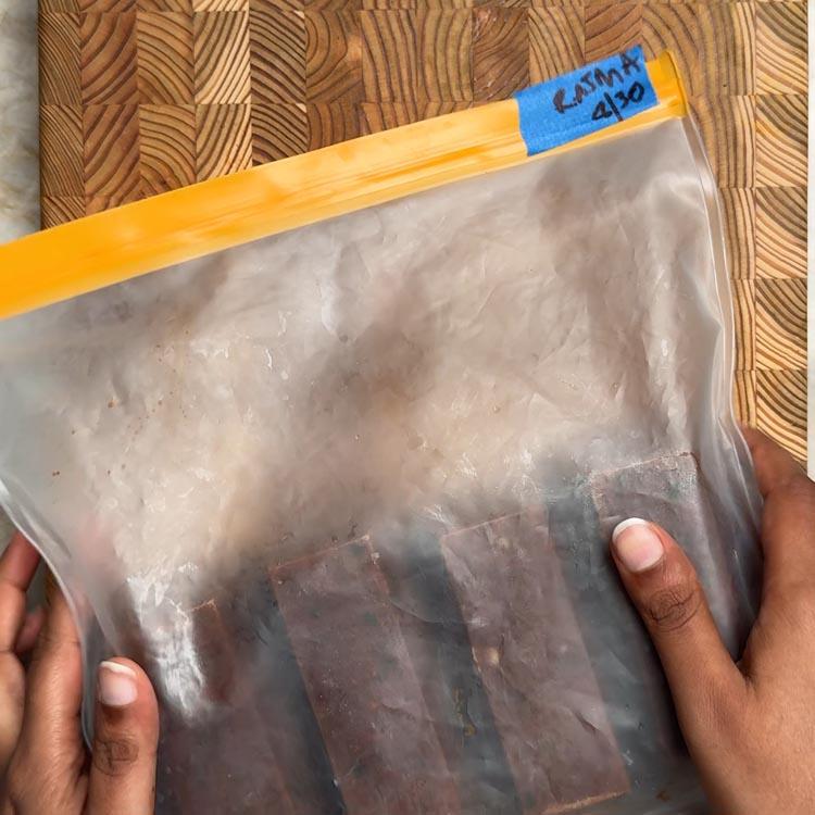 Hands holding clear freezer bag containing frozen curry portions with blue label