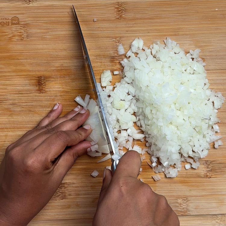 Uniformly diced white onions on bamboo cutting board with sharp knife