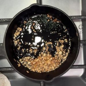 Minced garlic pieces bubbling in olive oil in black cast iron skillet on stovetop