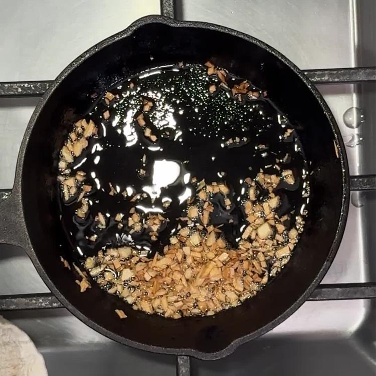 Minced garlic pieces bubbling in olive oil in black cast iron skillet on stovetop