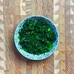 Tender dark green massaged kale salad base in blue ceramic bowl with black dot pattern on wooden surface