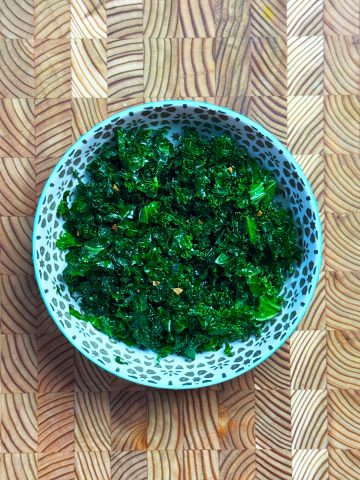 Tender dark green massaged kale salad base in blue ceramic bowl with black dot pattern on wooden surface