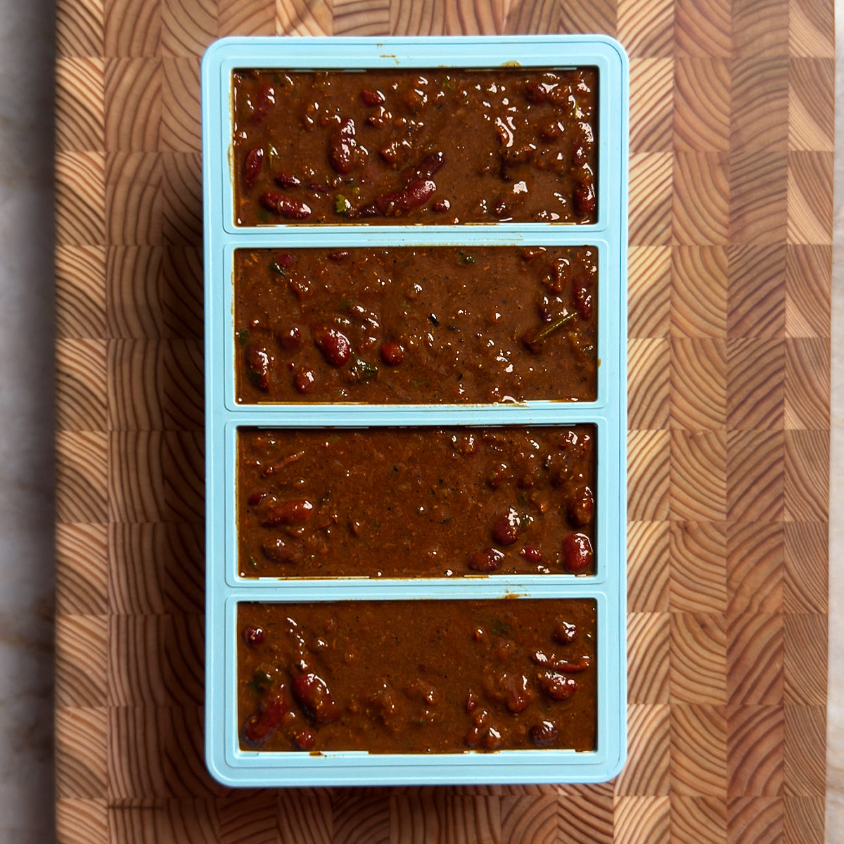 Rich brown rajma curry divided into four blue meal prep container compartments