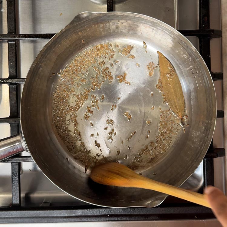 Oil heating in stainless steel pan with cumin seeds and bay leaf for tempering