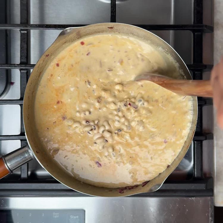 Soaked black eyed peas being stirred into the creamy coconut curry base in the pot