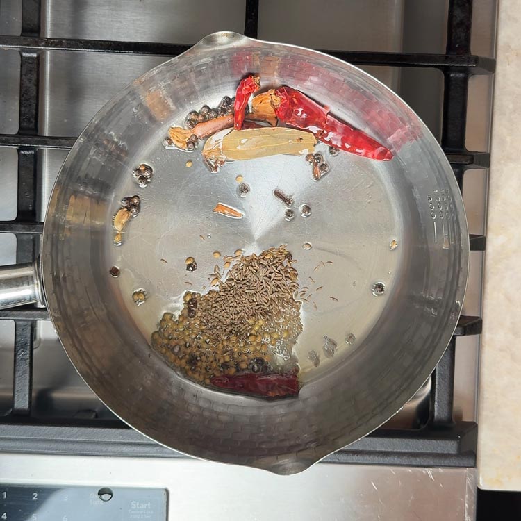 Golden cumin seeds and tan coriander seeds scattered in oil with red chilies and whole spices