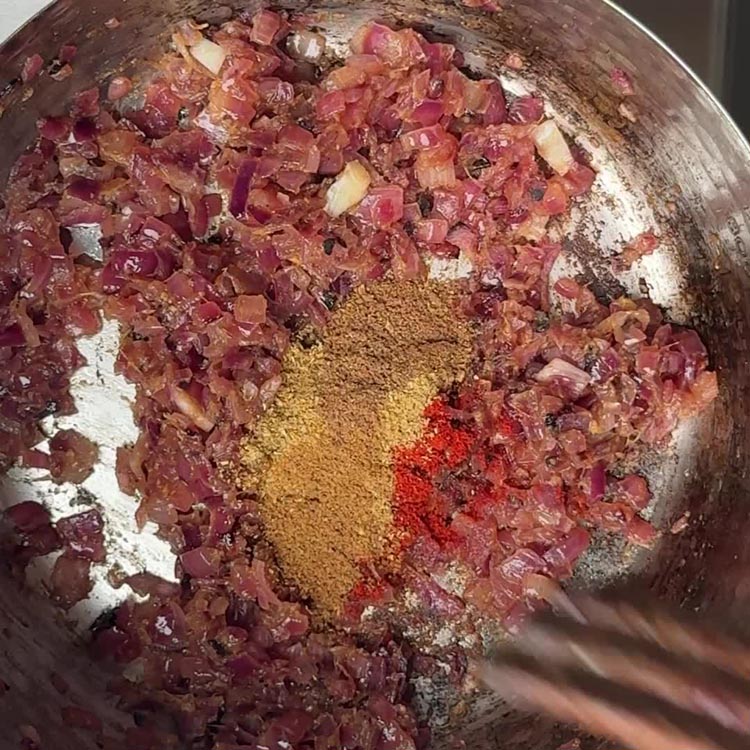 Red chili powder, tan coriander, garam masala, and cumin added to caramelized onions in pan