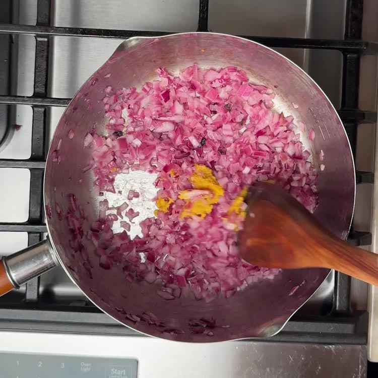 Golden pink onions with turmeric powder being stirred in, creating the aromatic spice base