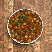 Authentic channa masala recipe in white patterned bowl on wooden background, garnished with coriander