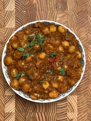 Authentic channa masala recipe in white patterned bowl on wooden background, garnished with coriander
