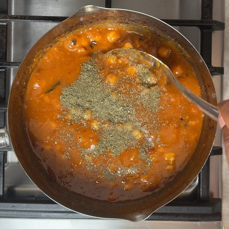 Golden chickpeas floating in orange curry with green kasuri methi leaves sprinkled on top