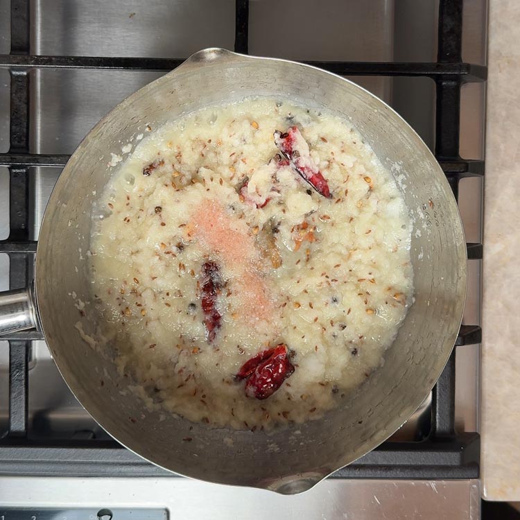 Pale translucent onion puree cooking in pan with red chili and visible cumin seeds