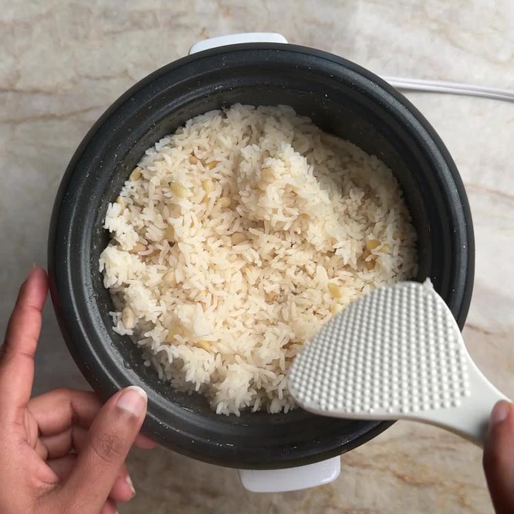 Silicone spatula scooping fluffy white rice dotted with golden pine nuts