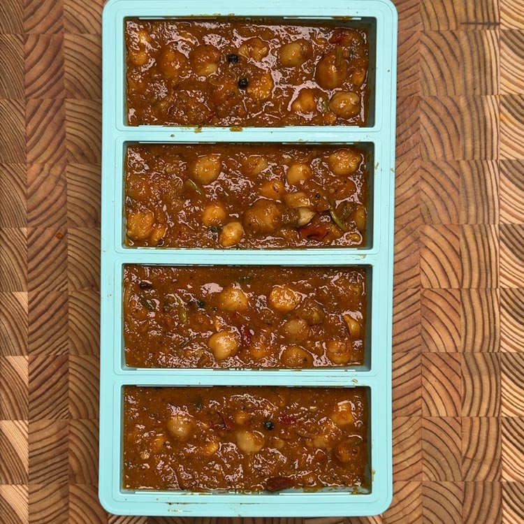 Four equal portions of brown chickpea curry stored in turquoise silicone freezer tray