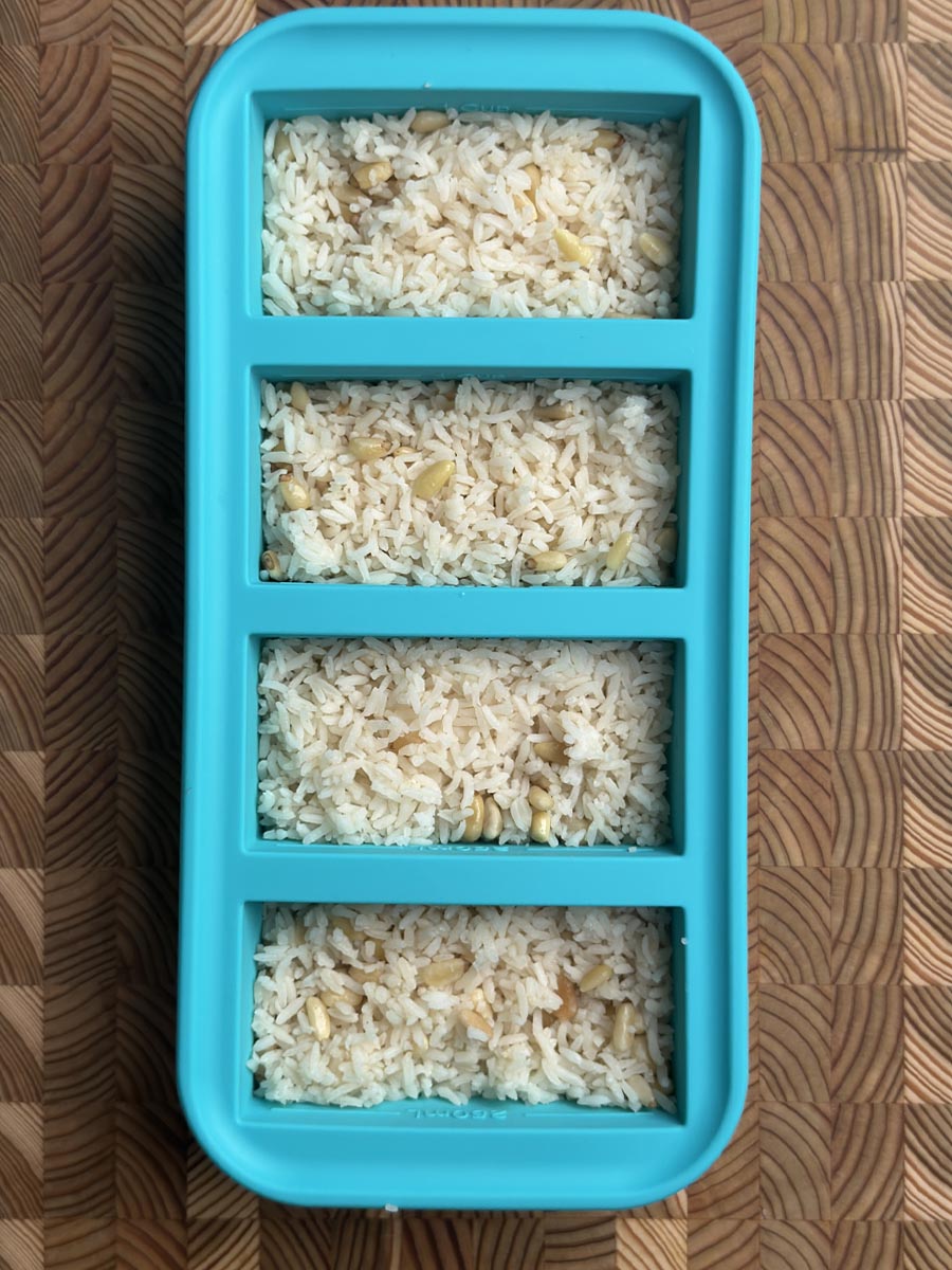 Four sections of turquoise Souper Cubes container filled with cooked pine nut rice, ready for freezing