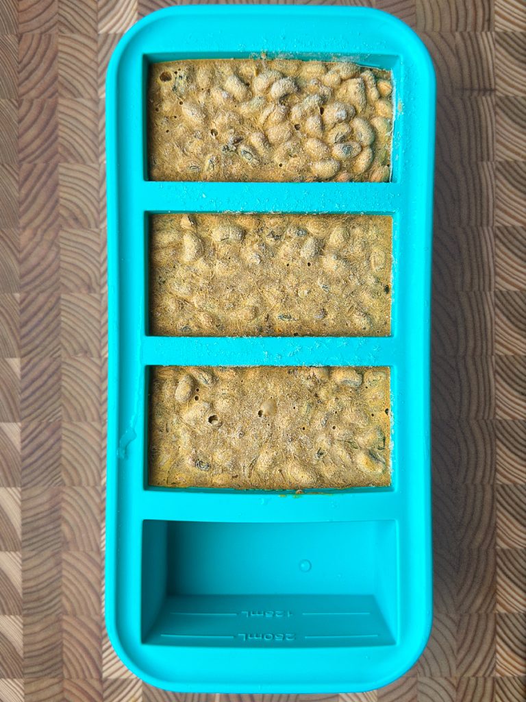 Three rectangular portions of curry mixture set in a turquoise freezer container for meal prep storage