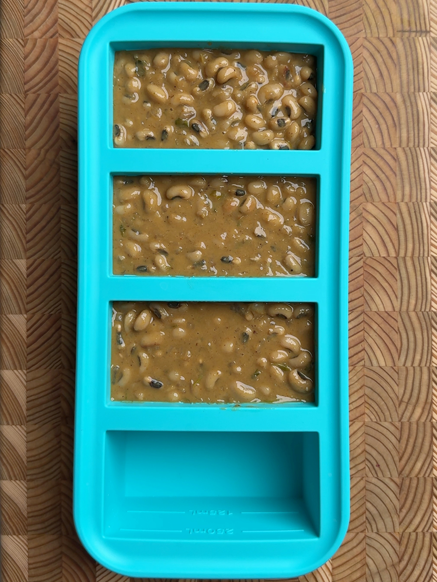 Three compartments in a turquoise freezer tray filled with portioned curry, ready for meal prep storage
