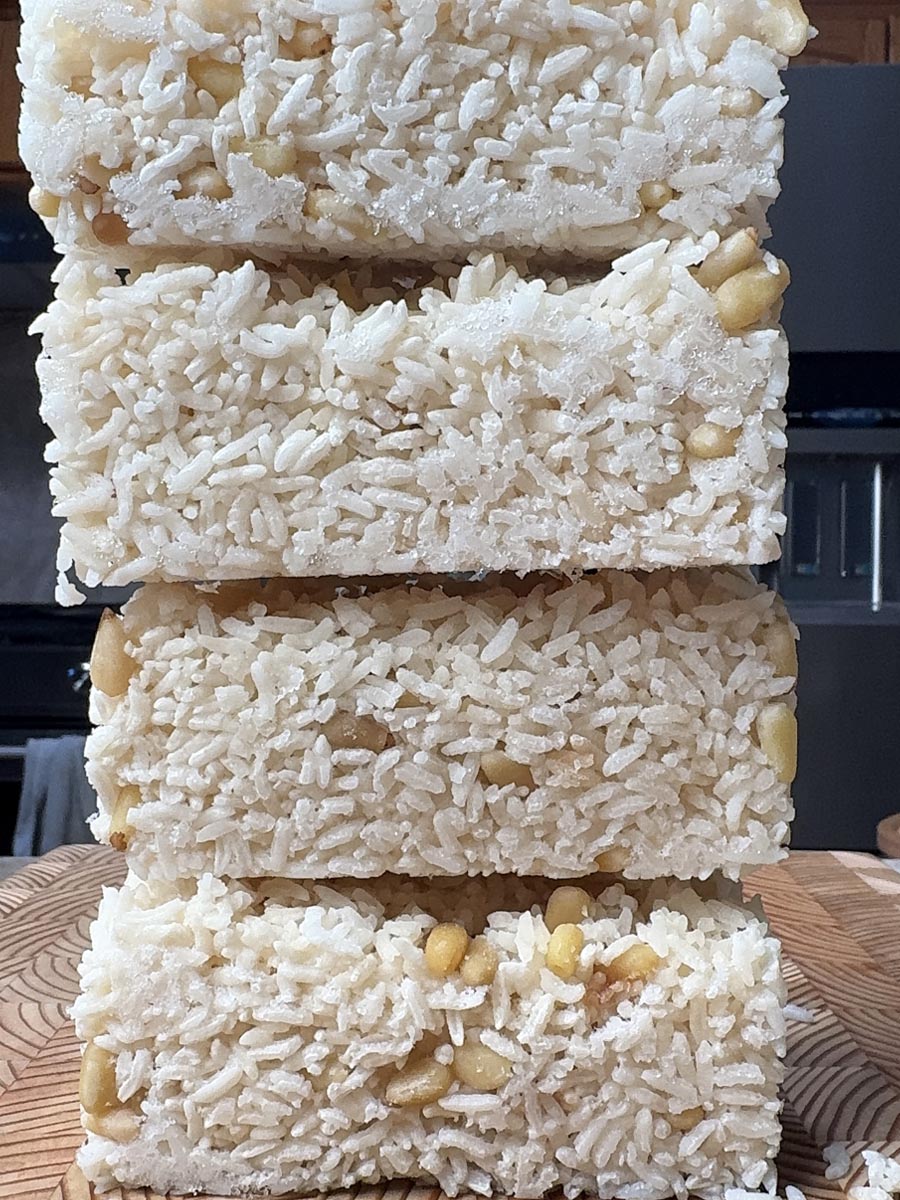 Four stacked frozen rice portions with visible pine nuts, white and pale yellow coloring from broth