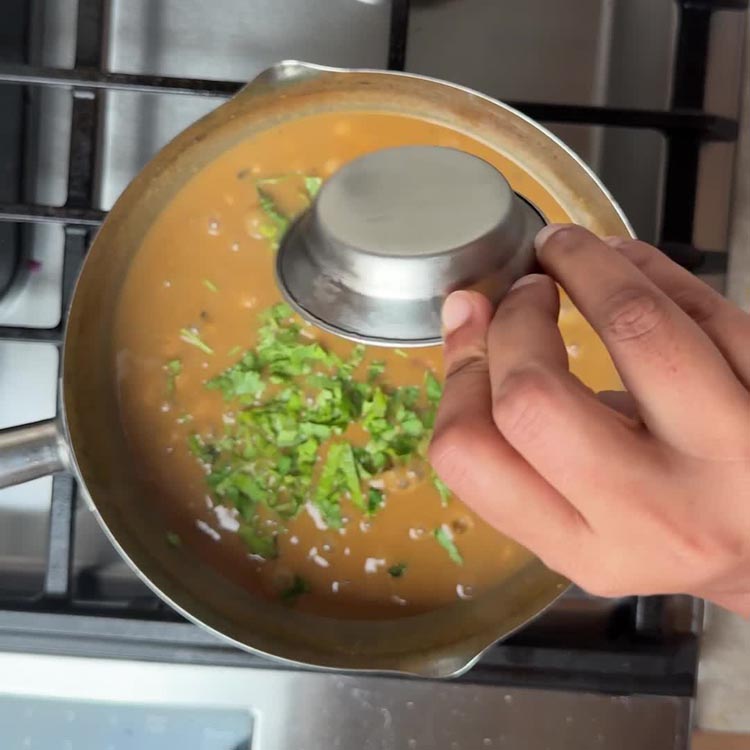 Fresh coriander leaves being sprinkled over finished curry