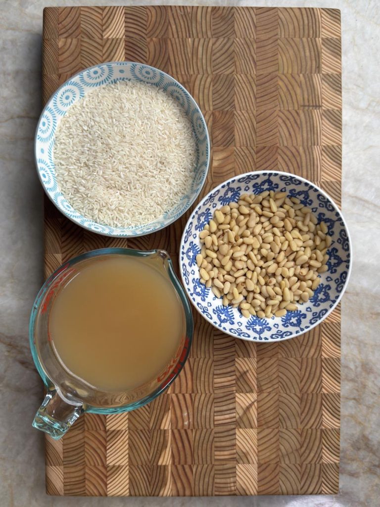 White rice in porcelain bowl, pine nuts in decorative dish, chicken bone broth in glass measuring cup