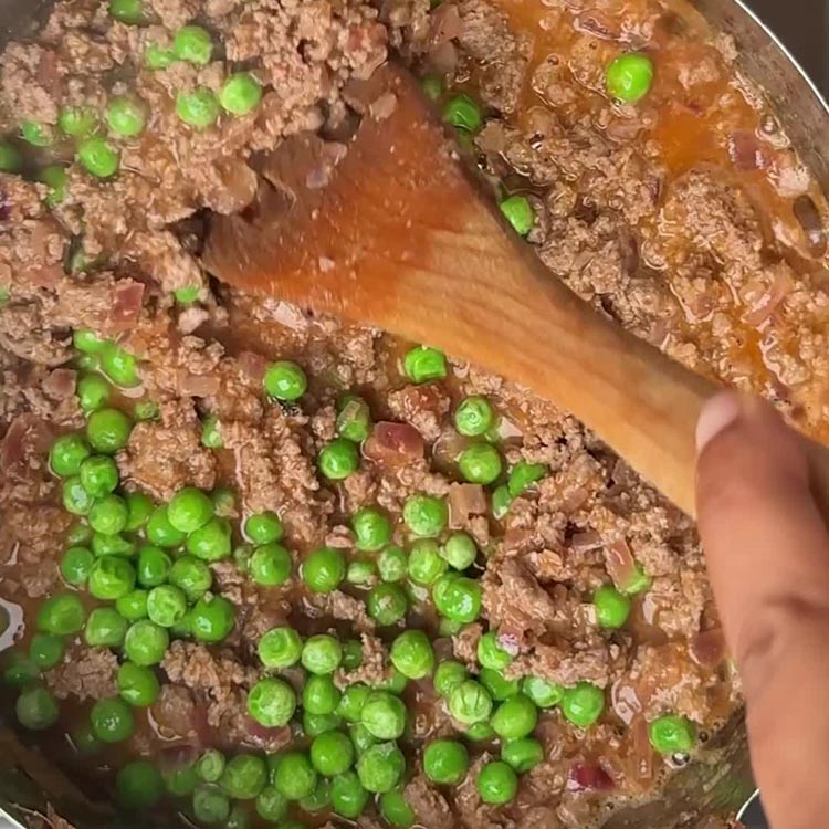 Cooked lamb mince with bright green peas and orange tomato paste in bubbling pan
