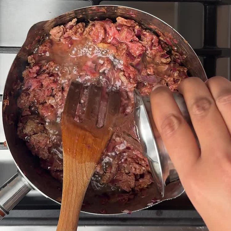 Raw ground lamb being mixed with water and spiced onions, fork breaking up meat clumps