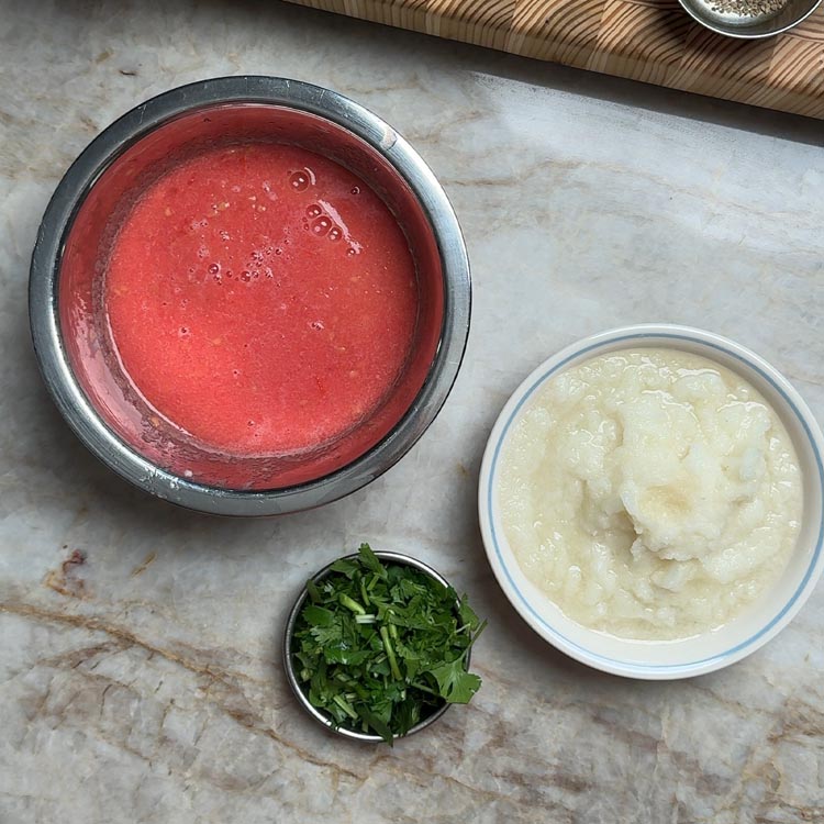 Smooth red tomato puree and pale onion puree in stainless steel bowls with chopped green coriander