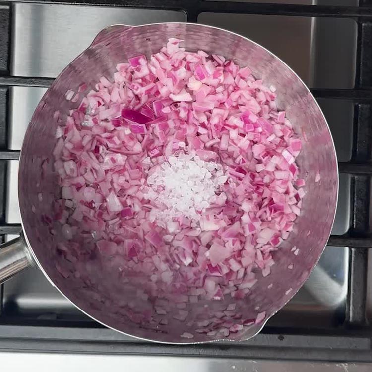 Chopped pink onions mixed with white ginger garlic paste and salt in cooking pan
