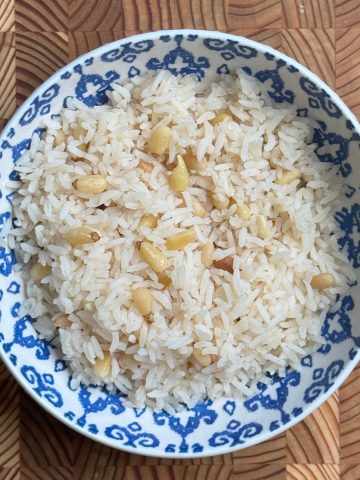 Pine nut white rice served in blue and white porcelain bowl, fluffy texture with golden nuts distributed throughout