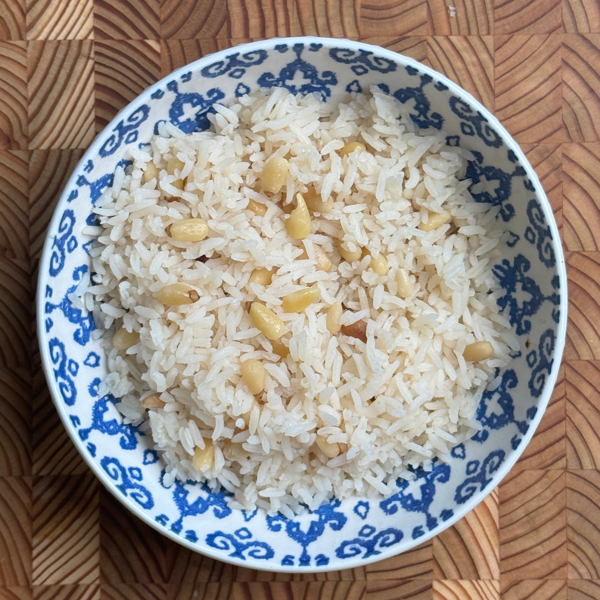 Pine nut white rice served in blue and white porcelain bowl, fluffy texture with golden nuts distributed throughout