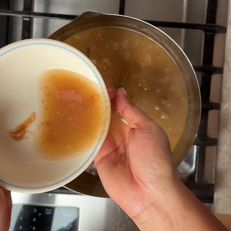 Tangy tamarind juice being poured into the simmering curry, adding brightness to the creamy base