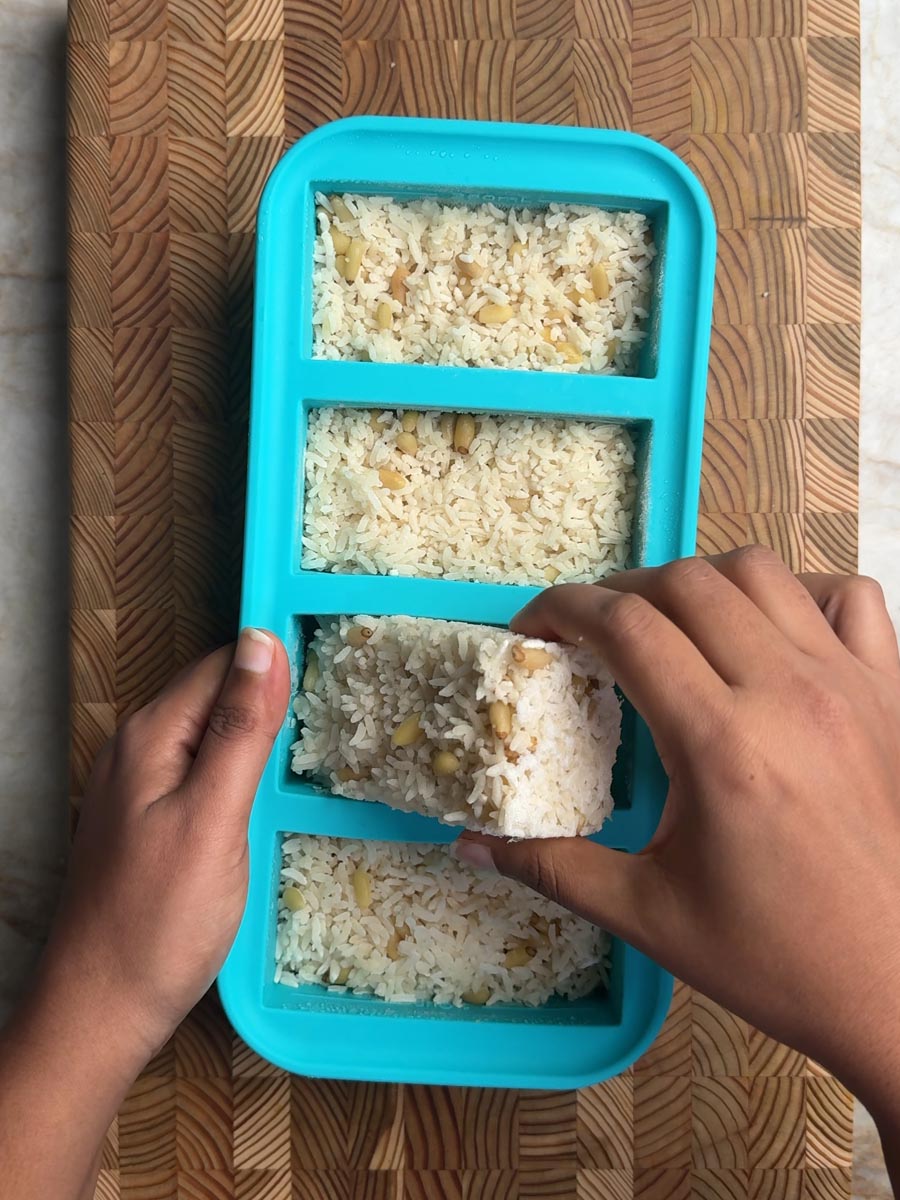Hand removing frozen rice portion from turquoise Souper Cubes, showing ease of meal prep storage
