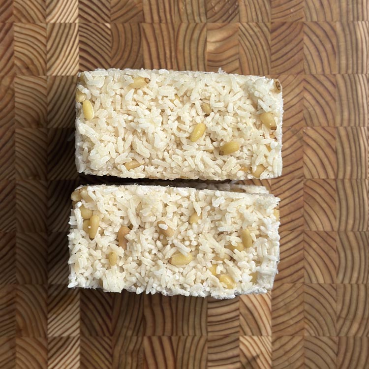 Two square-shaped frozen rice cubes studded with pine nuts on wooden board
