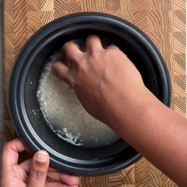 Hand rinsing white rice in rice cooker bowl, water running clear