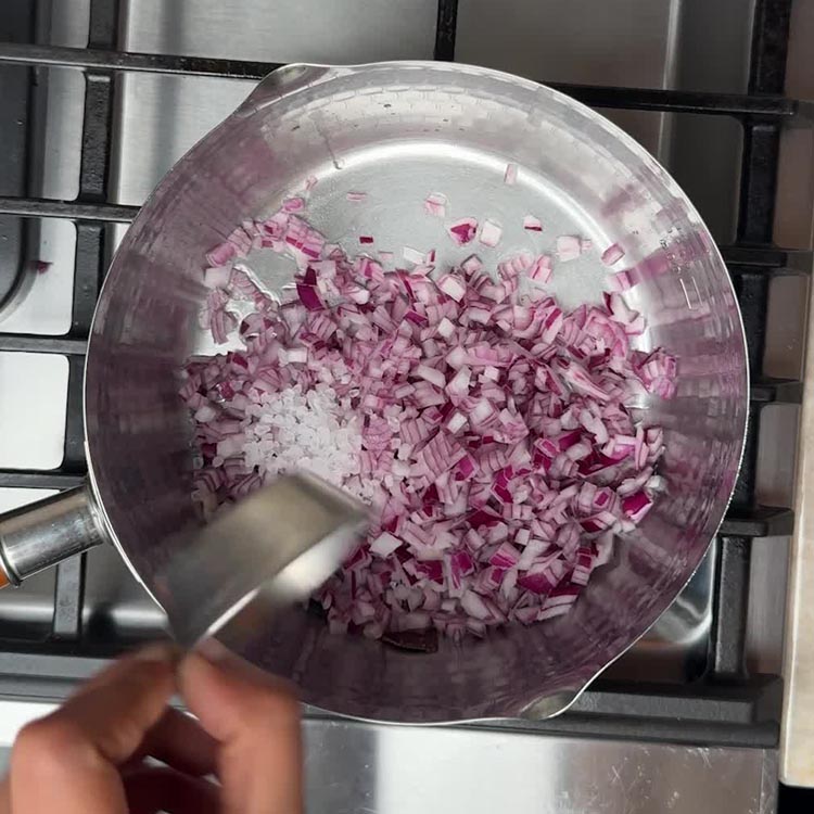 Finely diced red onions sautéing in hot oil in a steel pot, releasing aromatic flavors