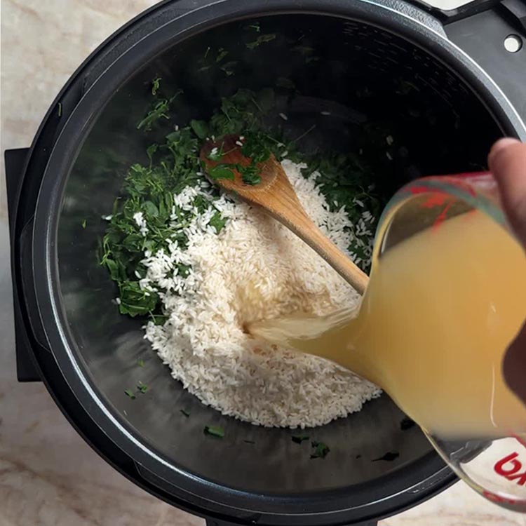 Pouring golden chicken bone broth from Pyrex measuring cup into Instant Pot with rice and wilted greens