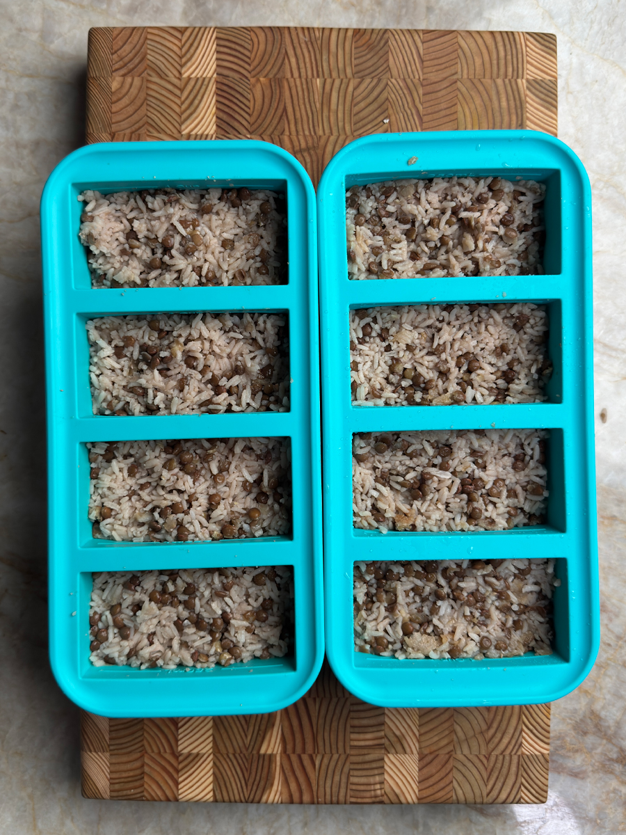 Eight portioned containers of cooked brown lentil and rice meal prep ready for the week