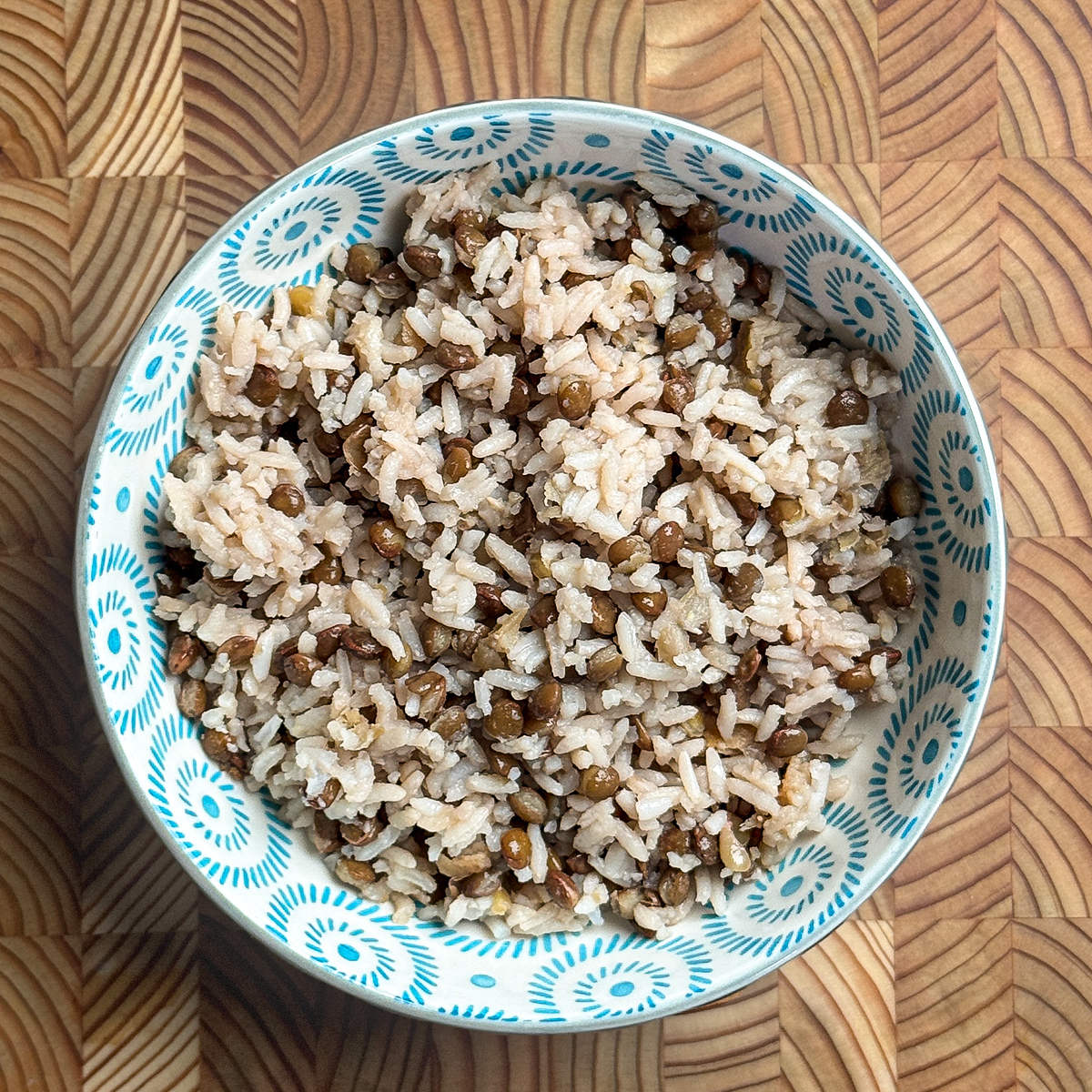 Fluffy cooked mixture of white rice and brown lentils in traditional blue patterned serving bowl