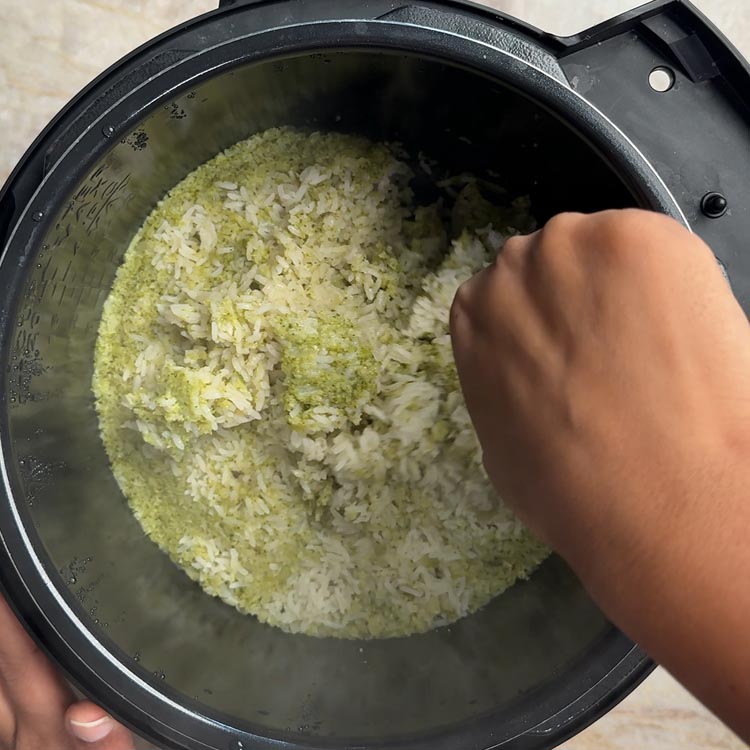 Hand fluffing cooked rice and broccoli mixture in pressure cooker with fork