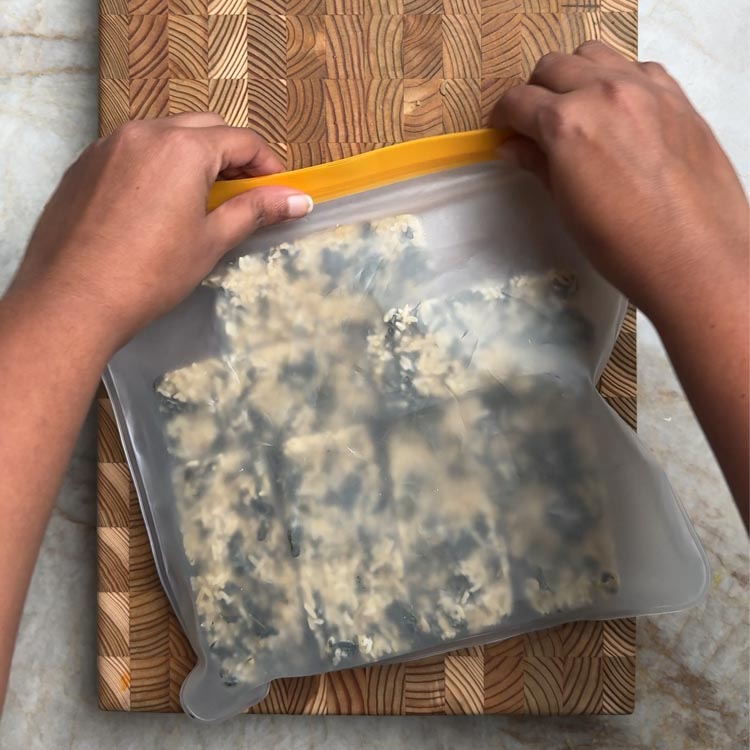 Hands sealing yellow topped freezer bag containing cooked rice with green moringa leaves for storage