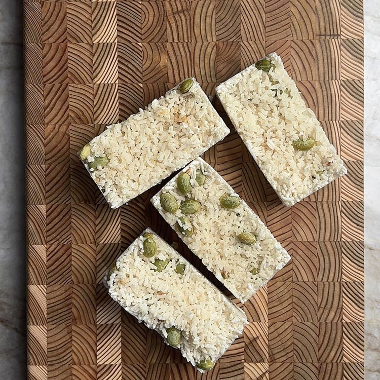 Four square-shaped frozen rice cubes studded with edamame on wooden board