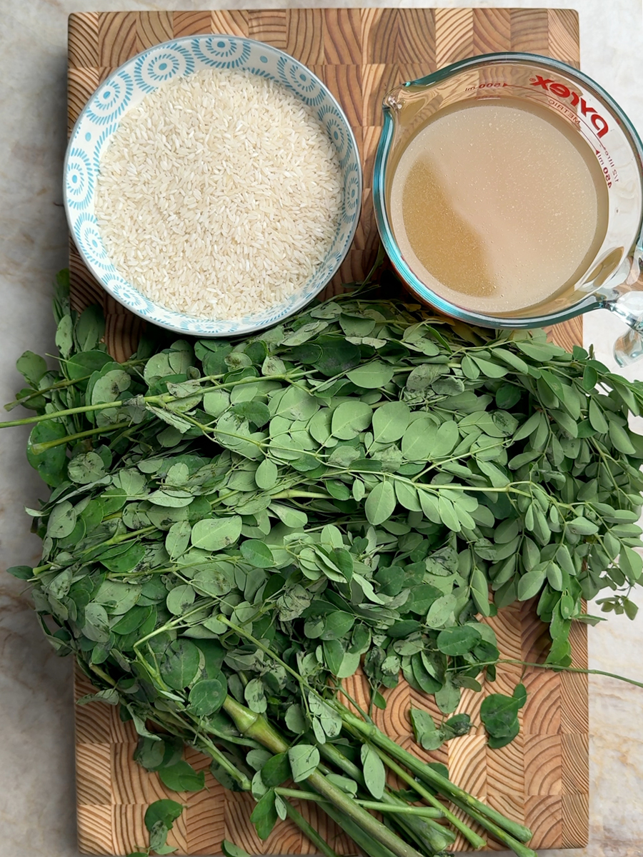 Fresh moringa leaves on branches, white basmati rice in blue bowl, and chicken bone broth on wooden cutting board