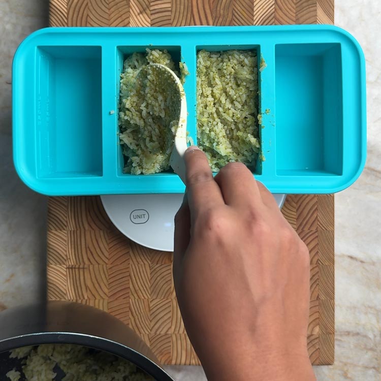 Spooning cooked rice into teal Souper Cubes silicone freezer tray on kitchen scale