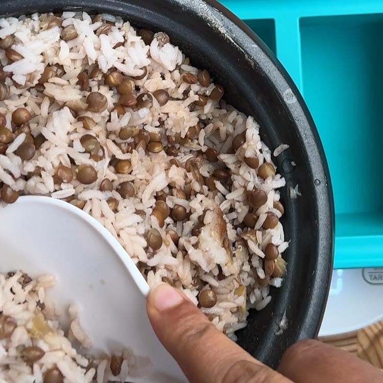 Scooping finished rice and lentil mixture into turquoise storage container for weekly meal prep