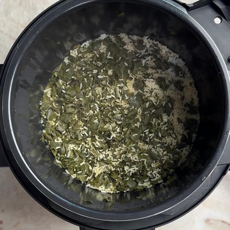 White rice grains mixed with dark green wilted moringa leaves in Instant Pot ready for pressure cooking