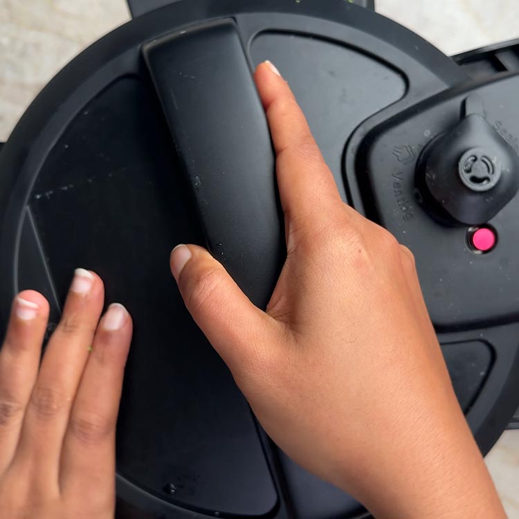 Hands closing black pressure cooker lid with valve visible in sealing position